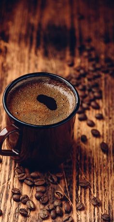 a cup of coffee sitting on top of a wooden table next to some coffee beans