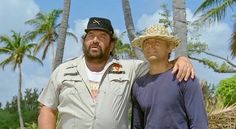 two men standing next to each other in front of palm trees