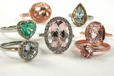 five different colored diamond rings on a white surface, one with an oval cut and the other with pear shaped diamonds