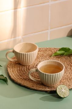 two cups of tea sitting on top of a place mat next to a lime slice