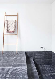 a bathroom with black and white tiles on the floor next to a wooden ladder that is leaning up against the wall