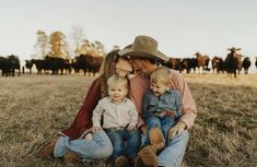 a man, woman and child sitting on the ground in front of cows