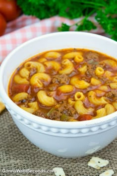 a white bowl filled with pasta and meat soup on top of a table next to bread