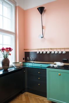 a kitchen with pink walls and wooden floors, black cabinets and an island in the middle