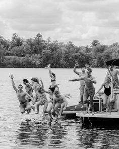 a group of people jumping into the water from a dock in front of some trees