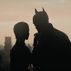 two people dressed as batman standing next to each other in front of a cityscape