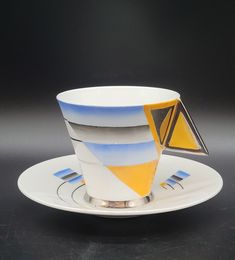 a cup and saucer with an abstract design on the side, sitting on a black surface