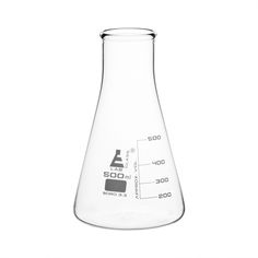 a flask filled with liquid sitting on top of a white table next to a measuring cup