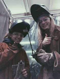 two women in jackets and helmets standing next to each other with one giving the thumbs up