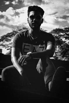 black and white photograph of a man sitting on the ground with clouds in the background