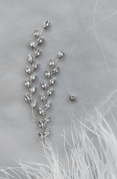 two pieces of jewelry sitting on top of a white cloth next to some silver feathers