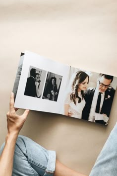 a person sitting on the floor holding up an open photo book with pictures of their wedding day