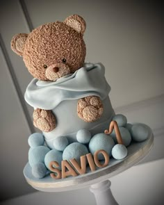 a teddy bear on top of a cake with blue frosting and balls around it