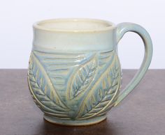 a ceramic mug with leaves on it sitting on a table