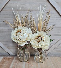 two glass vases with flowers in them on a wooden table next to a barn door