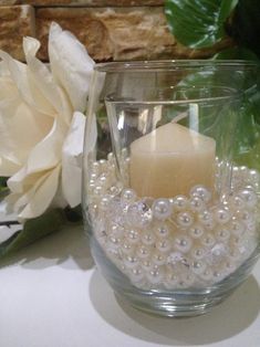 a candle that is sitting inside of a glass bowl with pearls on the rim and flowers in the background