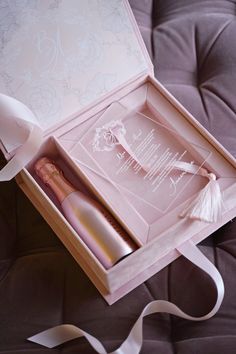 an open pink box with two bottles in it on a purple bed sheet and white ribbon