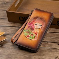 a woman's face is painted on the side of a brown leather wallet with flowers and leaves around it