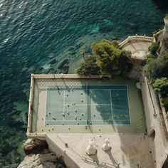 an aerial view of a tennis court on the water's edge with trees and rocks surrounding it