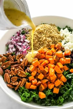 the dressing is being poured on top of the salad in a white bowl with kale, carrots, pecans and other ingredients