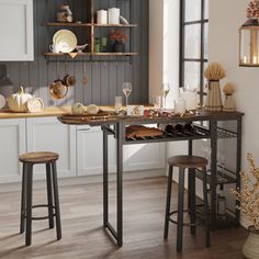 a kitchen with two stools and a table in front of the window, filled with dishes