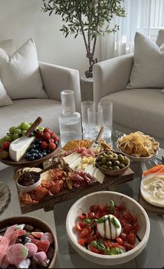 a table filled with different types of food on plates and bowls next to couches