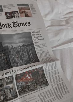 a newspaper laying on top of a bed covered in white sheets and pillows with the new york times front page