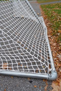 a metal net sitting on the side of a road next to some grass and leaves