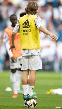 a soccer player in yellow and white uniform kicking a soccer ball on the field with other players behind him