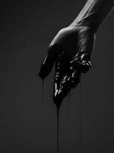 a person's hand with dripping black paint on it, against a dark background