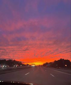 the sun is setting on an empty highway with cars driving down it and trees in the distance