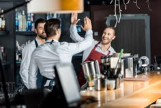 two men in aprons are standing at the bar and one man is raising his hand