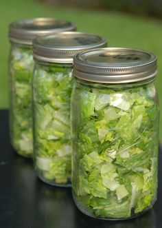 three mason jars filled with lettuce sitting on top of a black table next to each other