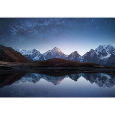 the night sky with stars above mountains and lake in foreground, reflected in still water