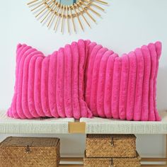 two pink pillows sitting on top of a white bench next to baskets and a mirror