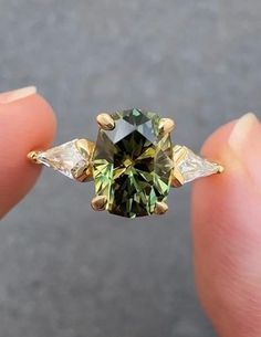 someone is holding a fancy ring with green and white diamonds on it's fingers