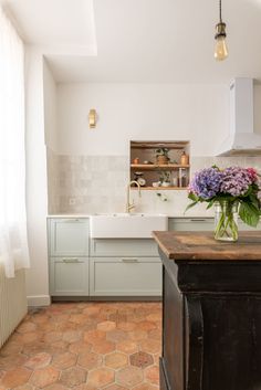 a vase with purple flowers sitting on top of a kitchen counter next to a sink