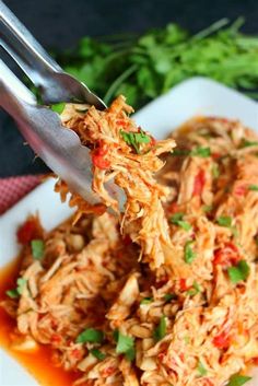 shredded chicken being lifted from a white plate with red sauce and garnished with parsley