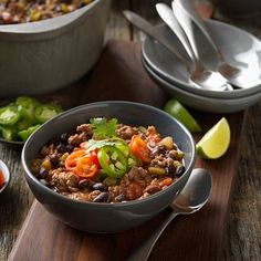 two bowls filled with chili and beans next to spoons on a wooden table top