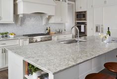 a kitchen with white cabinets and marble counter tops, an island sink and two stools