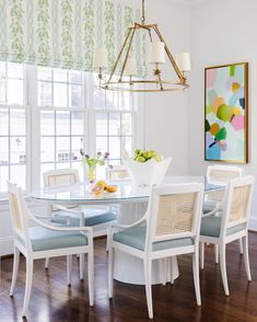 a white dining room table with blue upholstered chairs and a painting on the wall