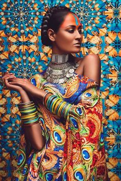 a woman with her hands on her hips wearing bracelets and an elaborate dress, standing in front of a colorful background