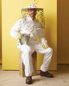 a man dressed as a beekeeper sitting on top of a wooden crate holding a bucket