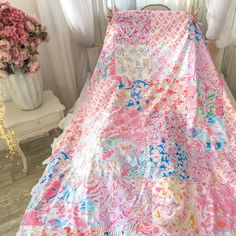 a pink and blue blanket sitting on top of a bed next to a vase with flowers