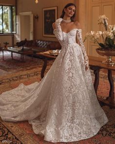 a woman in a white wedding dress standing on a rug with flowers and a table