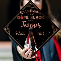 a woman holding up a black and white graduation cap that reads, imppologicic dove black teacher