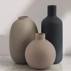 three different colored vases sitting on a white counter top, one is black and the other is grey