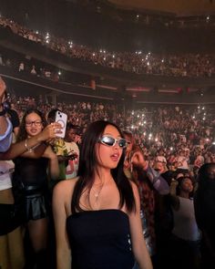 a woman wearing sunglasses standing in front of an audience at a concert with her cell phone up to her ear