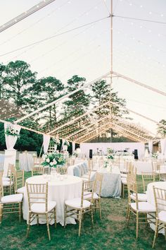 an outdoor tent with tables and chairs set up for a wedding reception in the grass