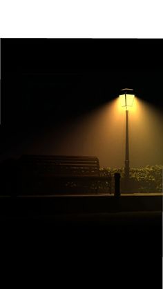 a bench sitting under a street light in the dark at night with fog on it